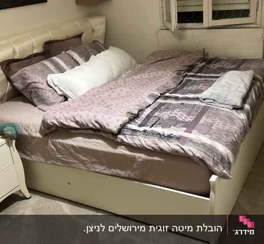 מיטה זוגית עם מצעים, כריות ושידה ליד